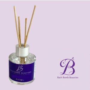 Reed diffuser bottle with multiple wooden sticks, purple label, and Bath Bomb Beauties logo on a pale lavender background.