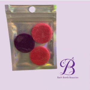 Clear resealable bag showing red and dark purple bath bombs; brand logo Bath Bomb Beauties appears in bottom-right.