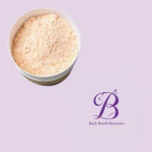 Powdery peach bath bomb powder in a white container on a lavender background with the Bath Bomb Beauties logo visible.