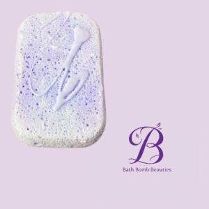 Lavender swirled white bath bomb with purple specks on a pale lavender background beside the bath bomb beauties logo