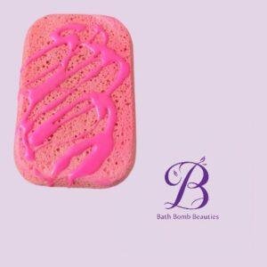 Pink rectangular sponge with bright pink drizzle on a light lavender background, next to the Bath Bomb Beauties logo.