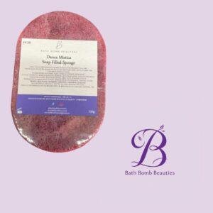 Pink oval bath bomb with a white label showing the Bath Bomb Beauties branding on a lavender background.