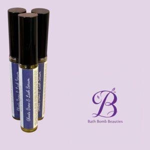 Three tall blue-labeled bottles with black caps standing upright on a lavender background, Bath Bomb Beauties logo in the bottom right.