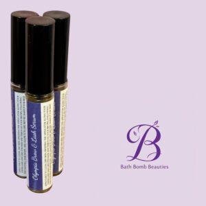 Three lip balm tubes with dark caps and blue labels stand upright on a lavender background, Bath Bomb Beauties logo visible to the right.