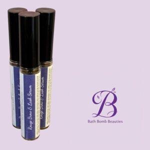 Three blue-labeled lip balm tubes with black caps standing upright on a lavender background, Bath Bomb Beauties branding visible.