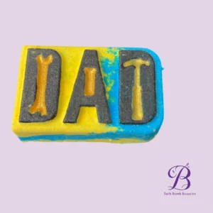 Colorful bath bomb with yellow and blue swirls embossed letters d a d on a gray insert against a pale lavender background watermark reads bath bomb beauties in the corner