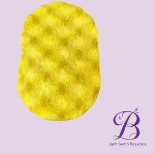 Yellow textured bath sponge on a light purple background with the bath bomb beauties logo in the bottom right