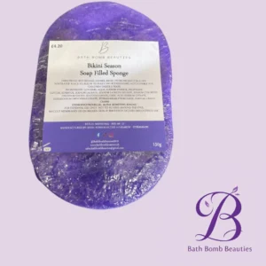 Purple soap sponge packaging labeled Bikini Season Soap Filled Sponge, 150g, Bath Bomb Beauties, on lilac background with logo in corner.
