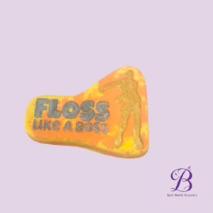 Orange-yellow bath bomb with the slogan 'FLOSS LIKE A BOSS' in gray letters and a gold running figure, on a lavender background (Bath Bomb Beauties logo).