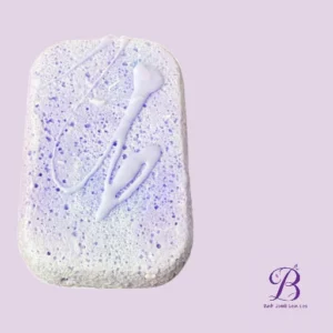 Lavender-scented bath soap bar with purple specks and white drizzle on a pale lavender background, brand logo in the corner.