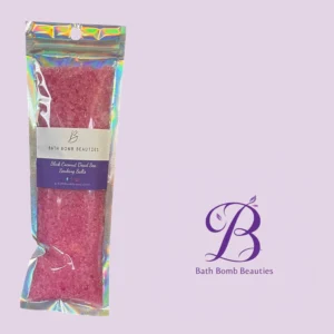 Pink bath salts in a shiny iridescent resealable pouch labeled bath bomb beauties and black coconut dead sea soaking salts against a lavender background