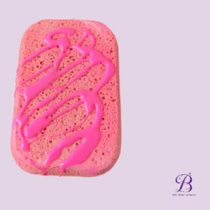 Pink sponge cake with magenta icing drizzled in zigzags on a pastel purple background with a small brand watermark in the corner