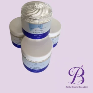 Open jar of Luxurious Whipped Soap (Black Coconut) by Bath Bomb Beauties on a lavender background with logo in the corner.
