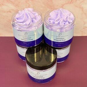 Three jars of lavender whipped soap (Luxurious Whipped Soap, Black Opium) with swirled purple texture on a pink surface, one jar open in front showpiece.