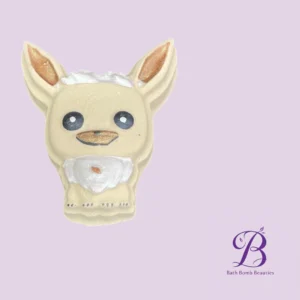 Cream-colored dog-shaped bath bomb with white beard and blue eyes on a lavender background; Bath Bomb Beauties logo in corner.