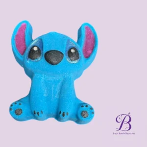 Blue Stitch-like plush figure sitting on a lavender background with Bath Bomb Beauties logo in the corner.