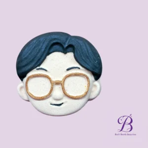 Partial view of a bath bomb character with blue hair and large gold rimmed glasses on a light purple background bath bomb beauties logo bottom right