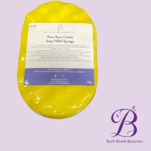 Yellow soap-filled sponge with a label reading 'Bum Bum Cream Soap Filled Sponge' on a lavender background, featuring the Bath Bomb Beauties logo in the corner.