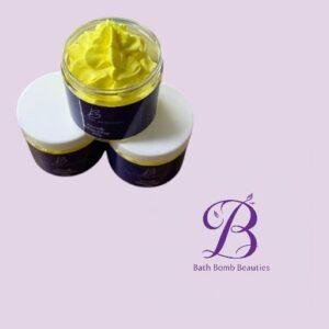 Three bath bomb jars on a pale lavender background, one open with bright yellow whipped bath product, with Bath Bomb Beauties logo nearby.