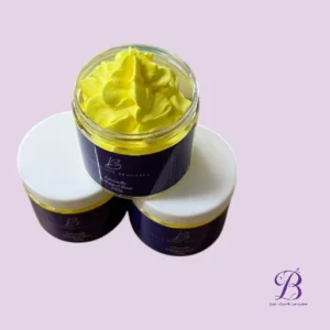 Three purple cosmetic jars with white lids and a bright yellow whipped cream/body butter open in the top jar, set against a lavender background with a logo in the corner.