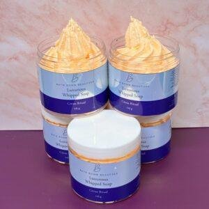 Jarred Luxurious Whipped Soap by Bath Bomb Beauties, Citrus Ritual scent, with peachy whipped swirls atop blue labels in a stack arrangement