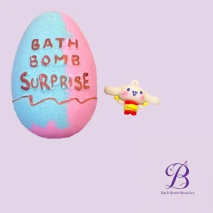 Colorful marbled bath bomb with 'BATH BOMB SURPRISE' written on it and a small bunny figure beside it (lavender background). The Bath Bomb Beauties logo appears bottom right.