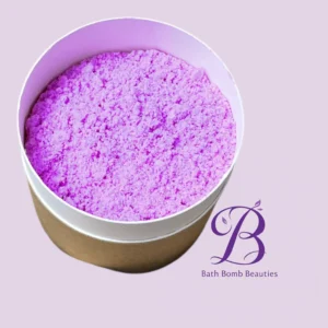 Purple bath bomb in a white-topped paper container on a lilac background; Bath Bomb Beauties logo visible nearby.