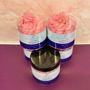 Three pink whipped soap jars labeled Bath Bomb Beauties Luxurious Whipped Soap Fakher Rose on a purple surface, arranged in a cluster with two jars behind and one in front.