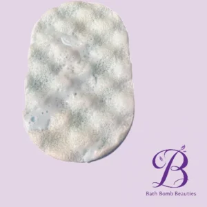 Oval bath bomb covered in bubbly foam on a lavender background with a 'Bath Bomb Beauties' logo in the corner.
