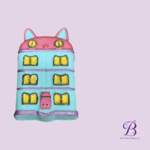 Whimsical cat shaped bath bomb turquoise with a pink top yellow lit windows set against a lavender background