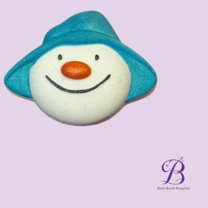 Snowman-shaped bath bomb with a turquoise hat and orange nose on a lavender background (Bath Bomb Beauties).