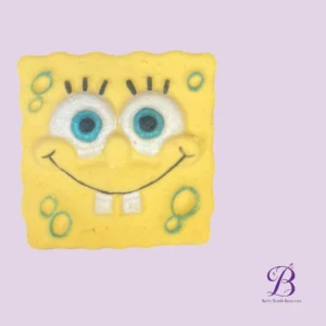 Bath bomb shaped like spongebob squarepants yellow with blue eyes and a big smile on a pastel purple background