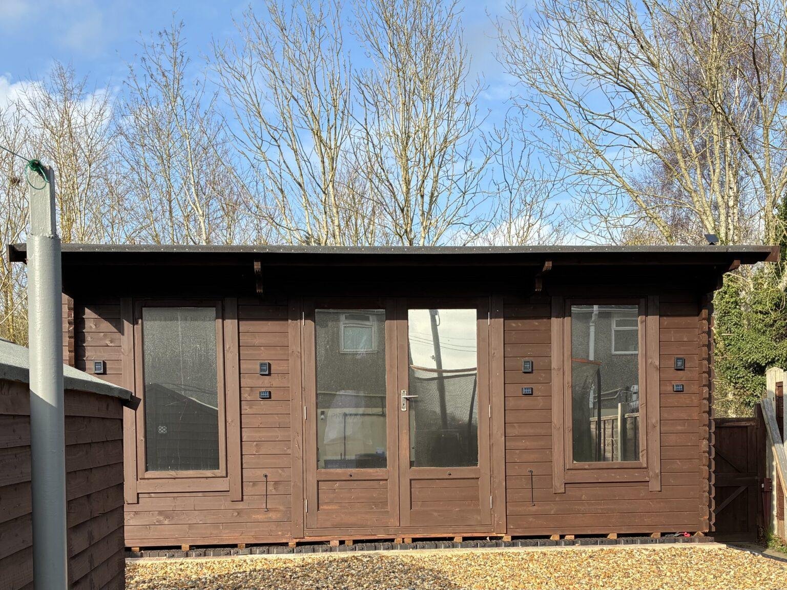 Brown wooden shed with three glass doors bare trees behind and a clear blue sky above