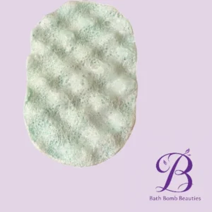 Oval bath bomb with pale green bubbles on a lavender background; Bath Bomb Beauties logo in the corner.