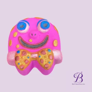 Cartoon style pink bath bomb with a big smile blue eyes and a gold polka dotted bow tie on a lavender background