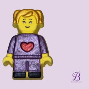 Lego style yellow figure with purple outfit and a red heart on the chest against a lavender background watermark bath bomb beauties in bottom right