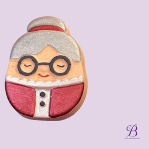 Close-up of a smiling cartoon bath bomb shaped like an elderly man with glasses on a lavender background (Bath Bomb Beauties).