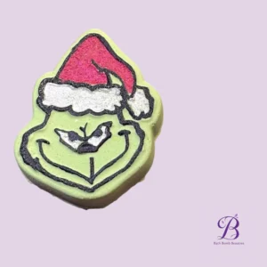 Smiling green bath bomb shaped like a face wearing a red Santa hat, with Bath Bomb Beauties logo in the corner