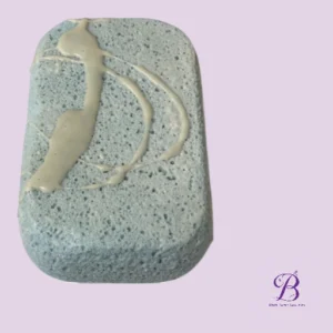 Rectangular light blue soap bar with cream drizzle on top against a lavender background with a small purple logo in the corner