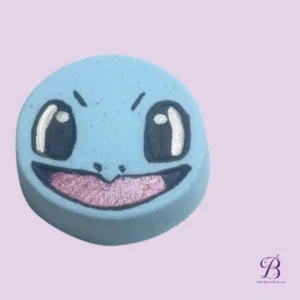 Blue round bath bomb with a cute smiling face and pink tongue, placed on a lavender background (Bath Bomb Beauties logo in the corner).