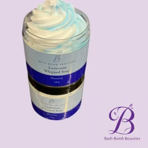 Jar of Bath Bomb Beauties Luxurious Whipped Soap with blue-and-white swirled cream, on a lavender background. The bottle shows a purple label and brand logo.