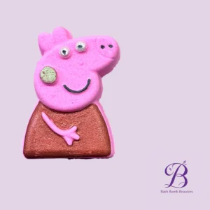 Pink pig shaped bath bomb with a silver snout and a smiling mouth on a lavender background bath bomb beauties logo visible in the corner