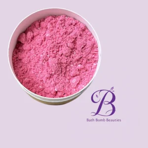 Close-up of pink bath bomb powder in a round tin on a lilac background with Bath Bomb Beauties branding.
