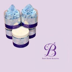 Two Bath Bomb Beauties whipped soaps in blue, in labeled jars, displayed side by side on a lavender background.