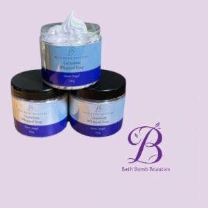 Three blue-labeled jars of Luxurious Whipped Soap (Snow Angel) stacked on a lavender background, with a Bath Bomb Beauties logo nearby.