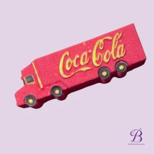 Pink Coca‑Cola truck-shaped bath bomb with gold logo, on a lavender background, branded by Bath Bomb Beauties
