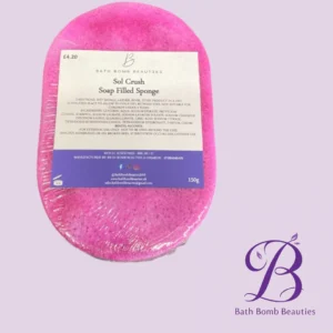 Pink oval soap bar labeled 'Sol Crush Soap Filled Sponge' from Bath Bomb Beauties, 150g, wrapped in plastic on a lavender background with the Bath Bomb Beauties logo in the bottom-right corner.