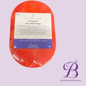 Red oval bath bomb with a white label reading 'Sol Summer Soap Filled Sponge' from Bath Bomb Beauties, placed on a pastel purple background with a purple brand logo in the corner.