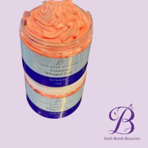 Jar of Bath Bomb Beauties Luxurious Whipped Soap in peach, coral color, on a lavender background with the brand logo nearby.