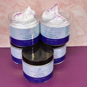 Three jars of Bath Bomb Beauties Luxurious Whipped Soap (Sparkling Lychee) with whipped-topped lids, arranged on a pink surface.